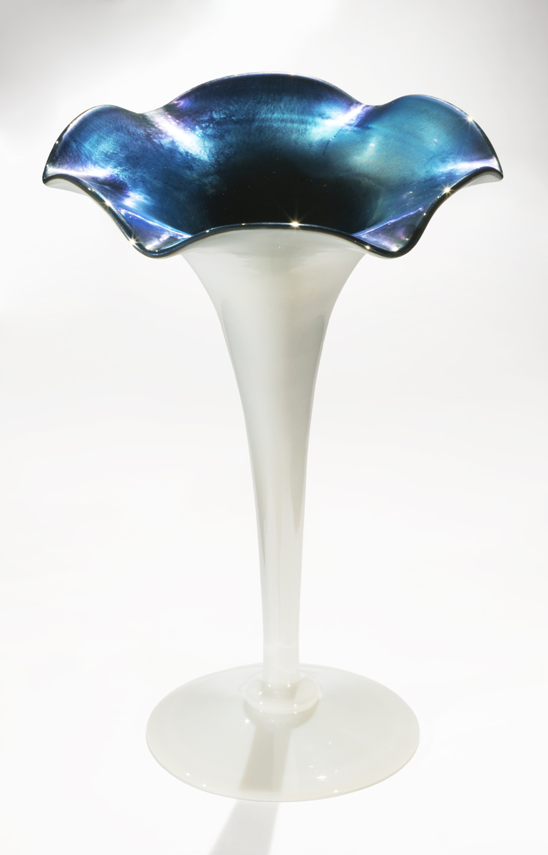 White vase, widening from thin base to flattened, flower-shaped top, which is iridescent blue inside