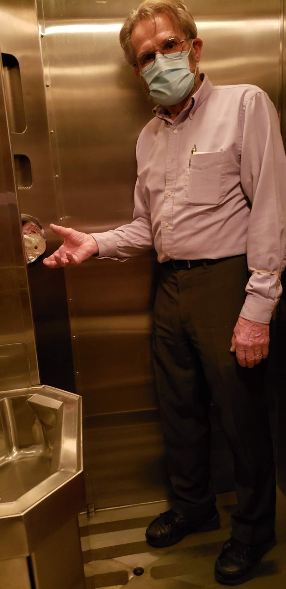 Man stands with hand next to knob in a stainless steel restroom containing a sink