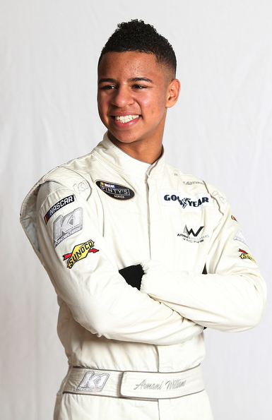 Armani Williams Smiling African American man with arms crossed, wearing white jumpsuit with a number of patches and logos