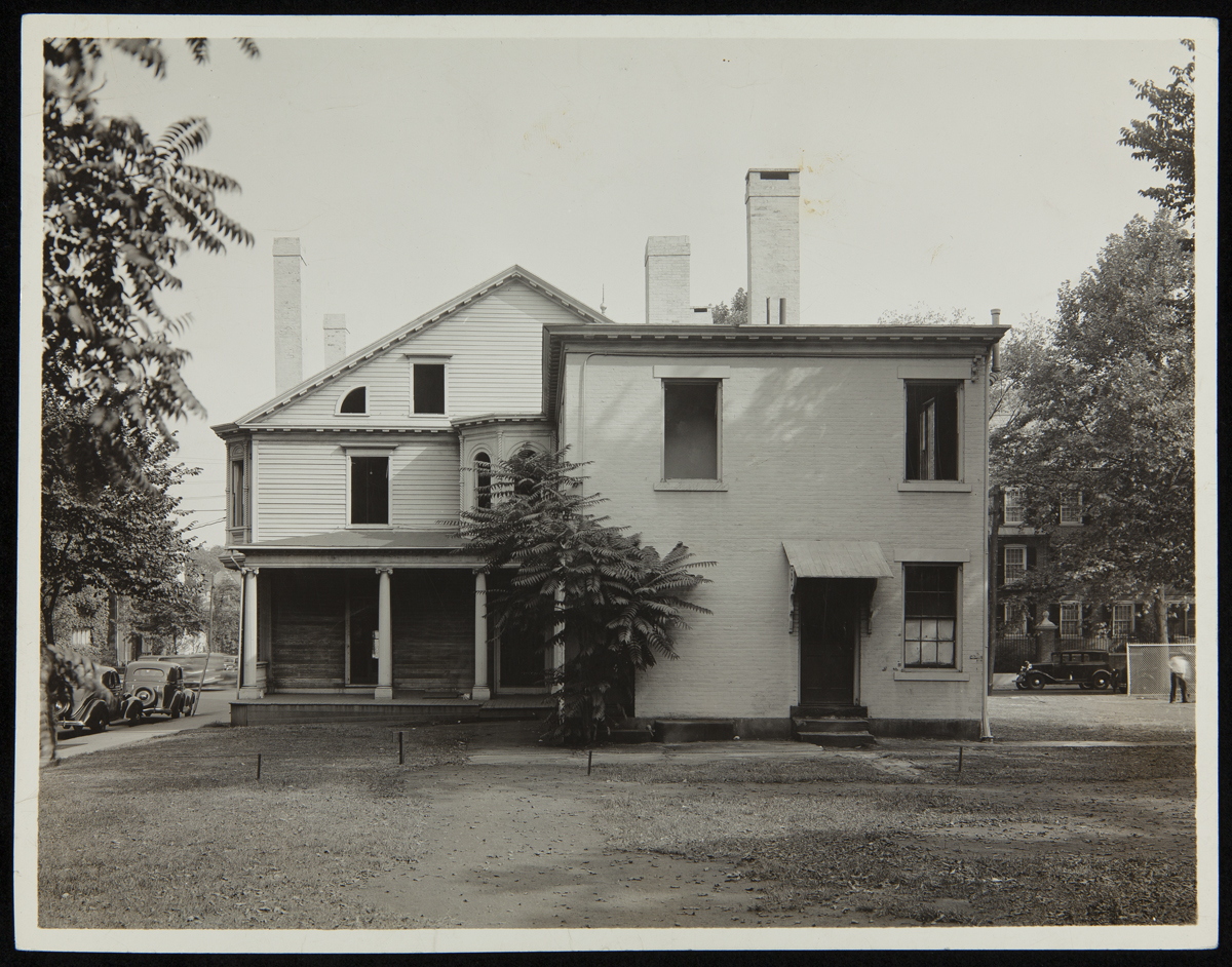 Back of two-story wooden building with porch, columns, and square addition to right side