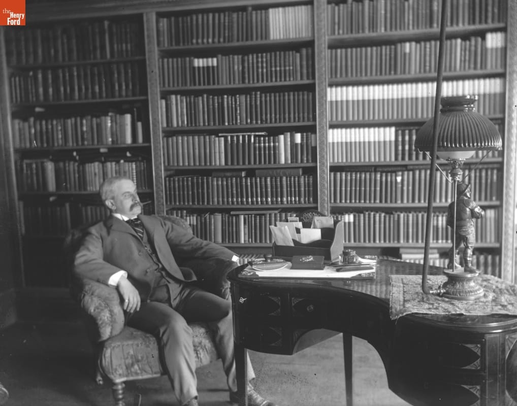 Photo taken by Jenny Young Chandler of a man sitting in an armchair next to a case of books in a library