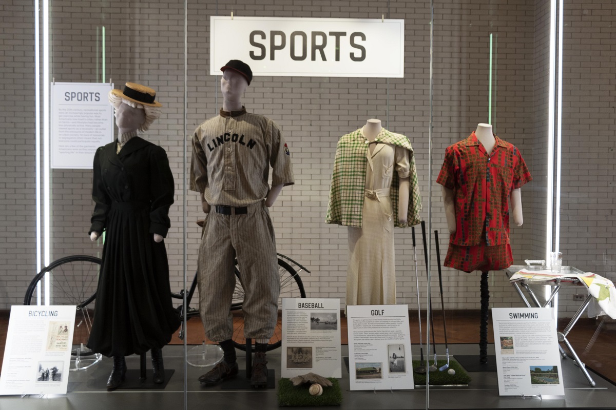 Large glass case with large label "Sports," other smaller labels, and four mannequins wearing various clothing
