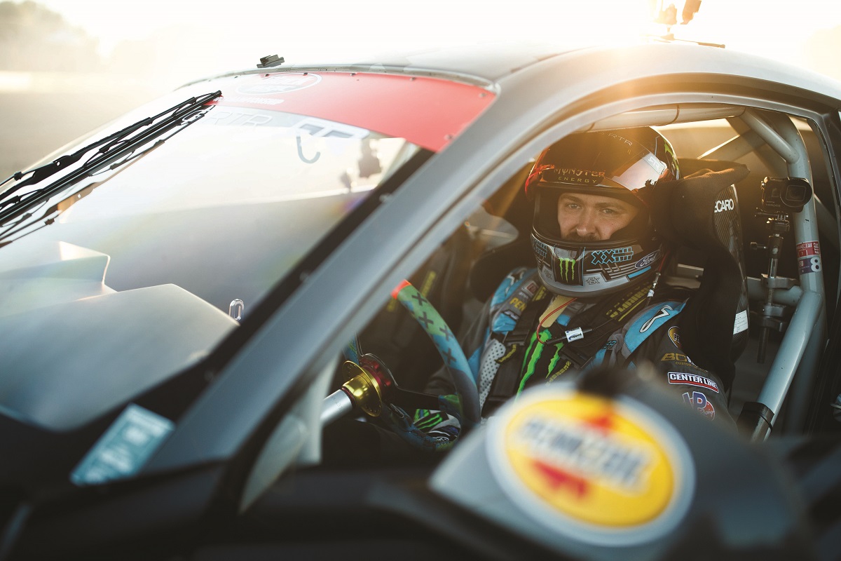 Tight shot of a man in racing helmet and jumpsuit sitting in race car sunlit from behind