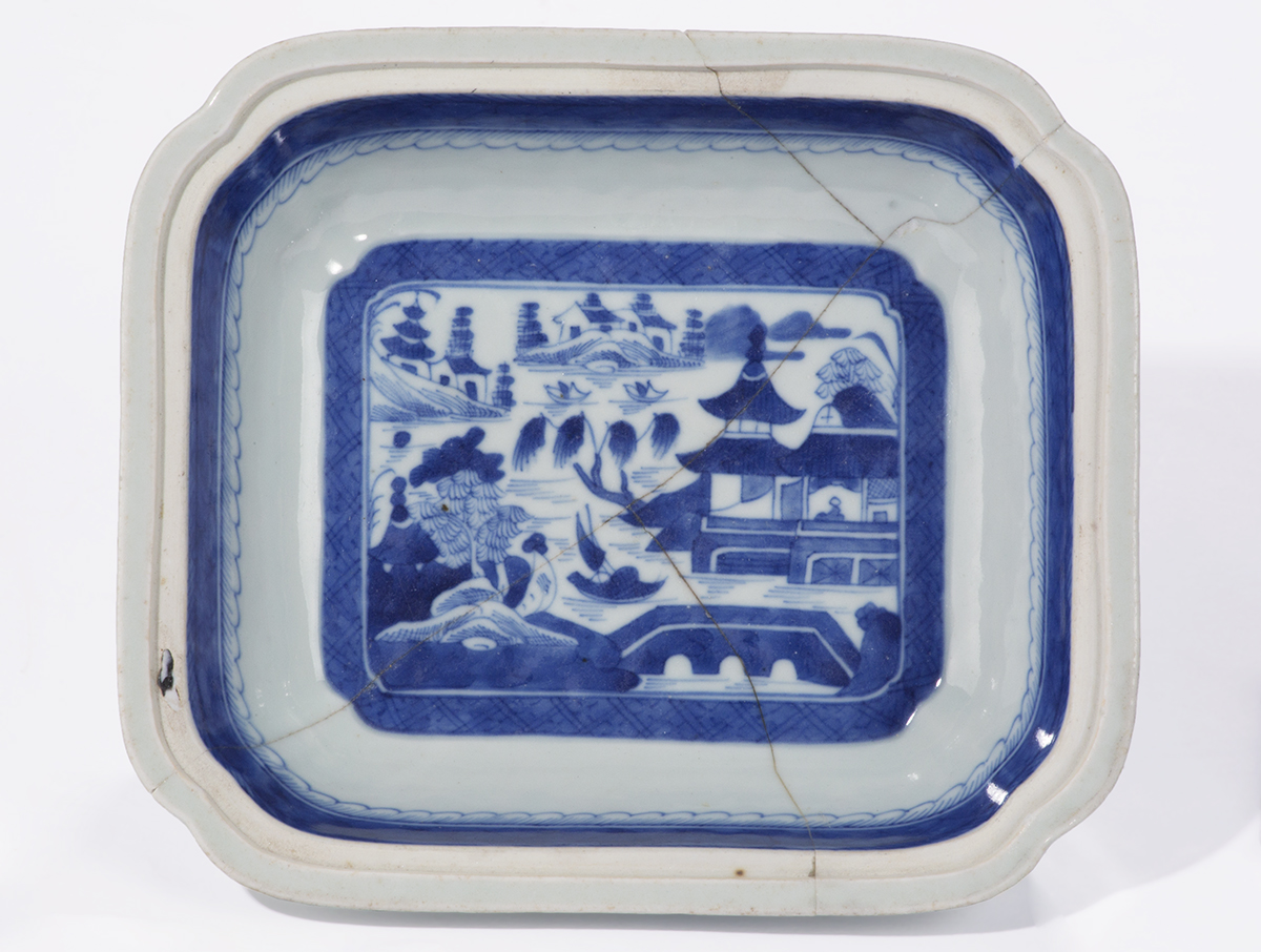 Head-on view of interior of shallow, rectangular bowl with blue stripe around rim and image in blue of landscape with building