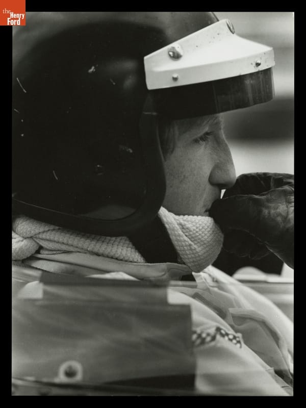 Close-up side view of man's head in crash helmet with a gloved hand to his mouth