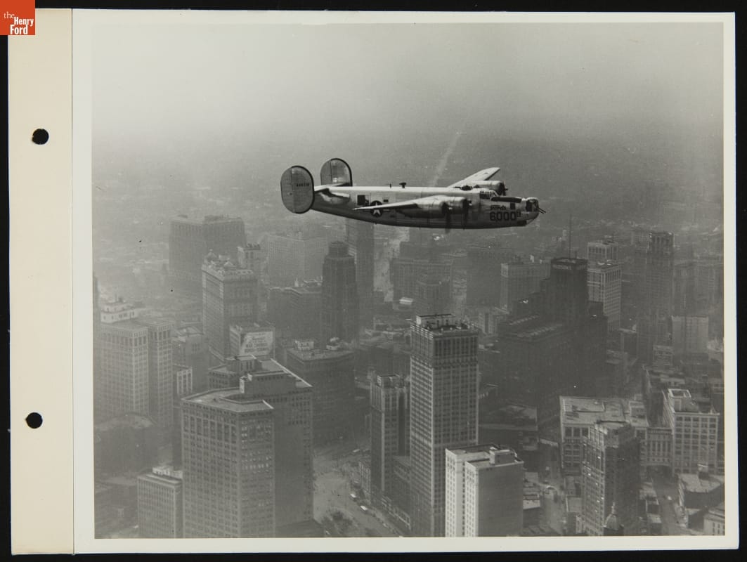 6000th Ford B-24 in Flight over Detroit, Michigan, September 13, 1944 Black-and-white image of airplane flying over tall buildings.