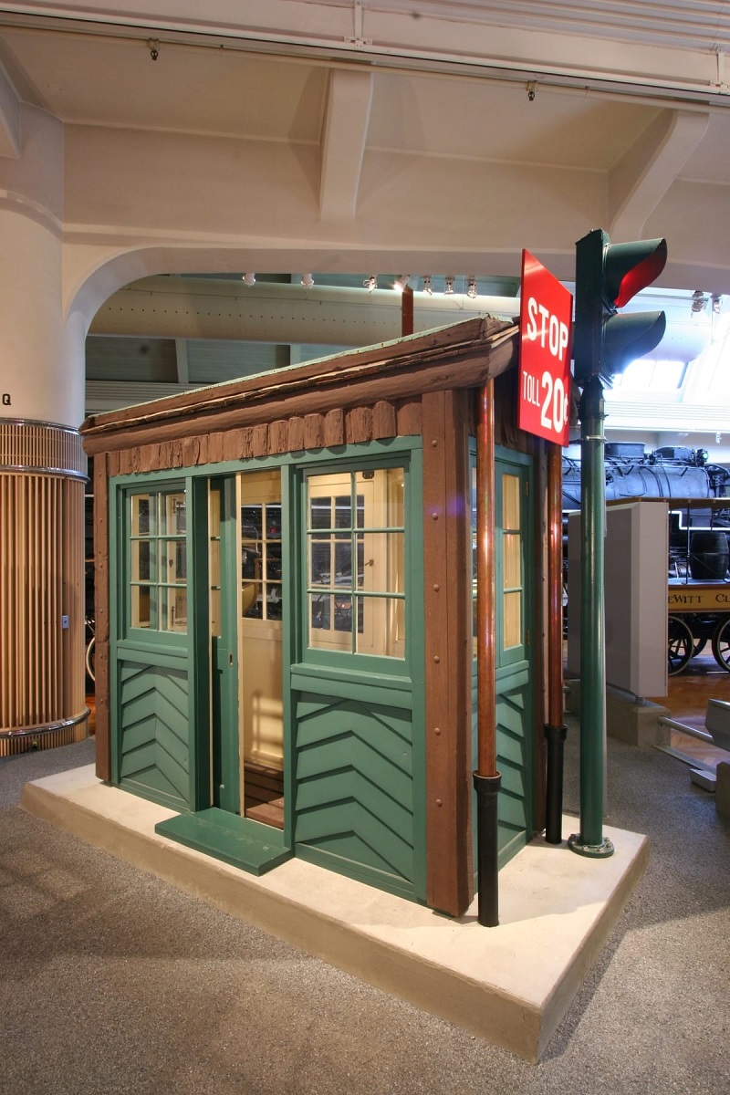 Very narrow brown and green wooden building with stoplight and "STOP TOLL 20 CENTS" sign 