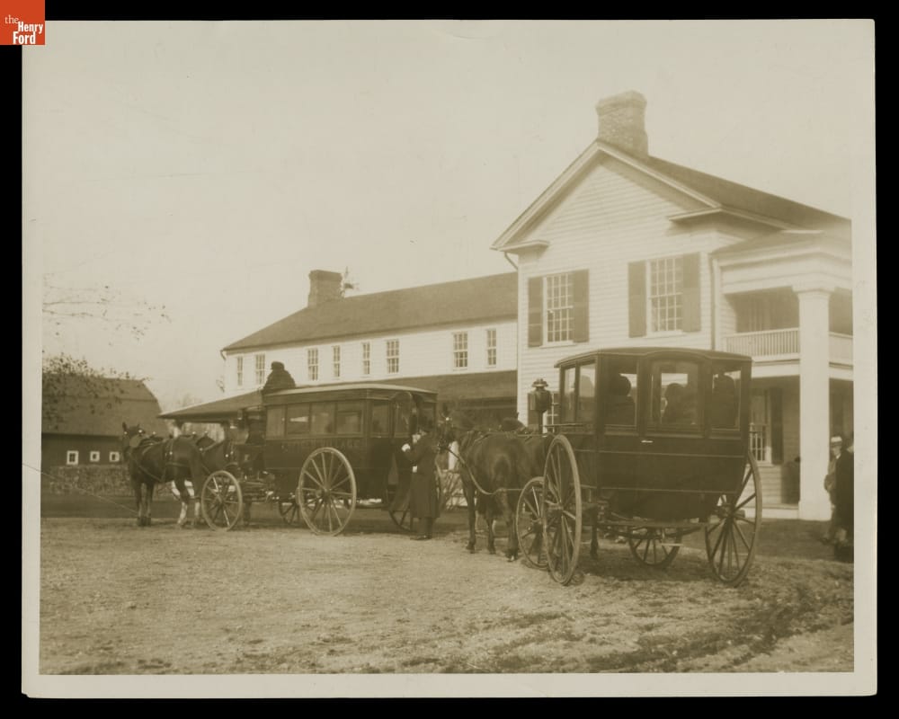 Enclosed carriages drawn by horses outside a two-story building