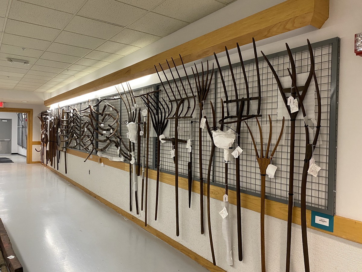Wooden rakes, yokes, and other items hang from a wire grid in a hallway