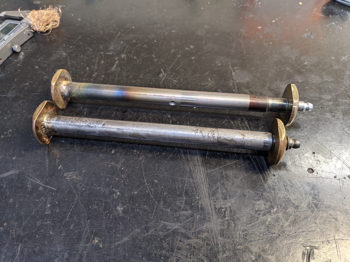 Two metal rods with gold stoppers on either end sit on a metal table