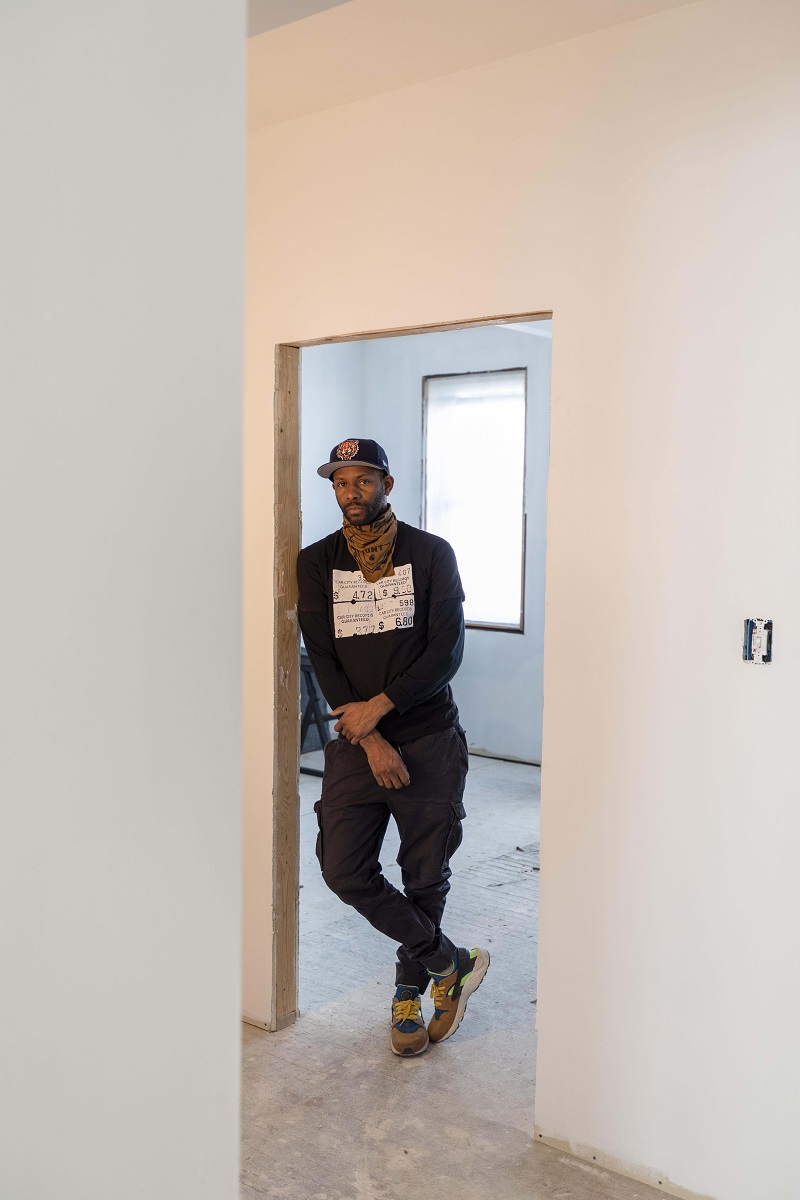 African American man leans in the doorway of an empty room that appears to be under construction
