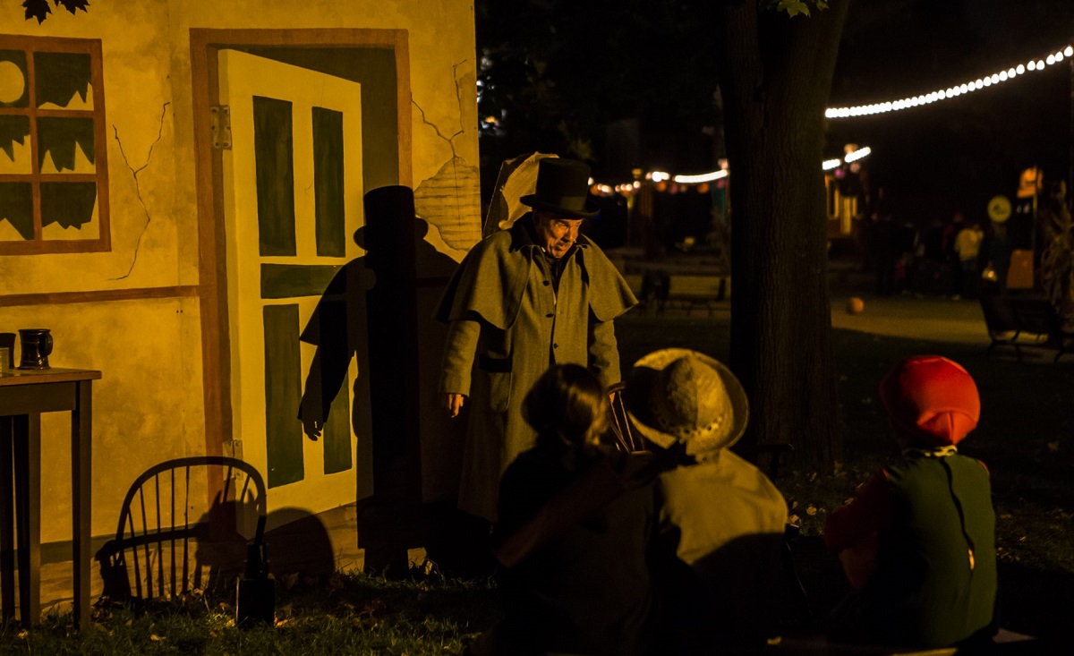 Anthony Lucas in "The Tell-Tale Heart" Man in overcoat and top hat stands in front of a backdrop of a building as seated people look on