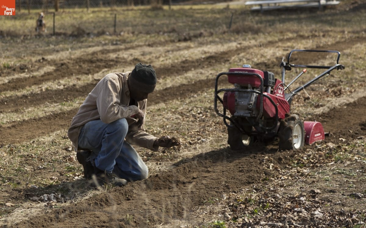 Melvin Parson Gardening during the Entrepreneurship Interview A Black man kneels in a field, examining soil, next to a tiller