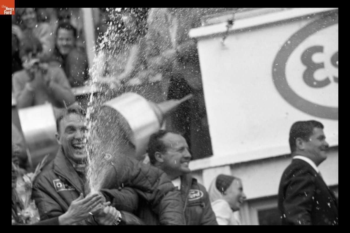 Dan Gurney and A. J. Foyt with Victory Champagne at the 24 Heures du Mans (24 Hours of Le Mans) Race, June 1967 Smiling man sprays champagne from a bottle as others look on