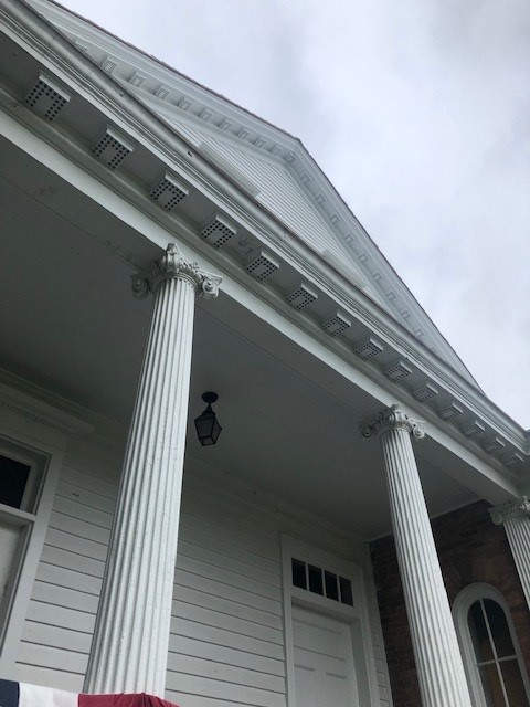 View, looking up from below, of white building porch with columns, topped with triangular gable