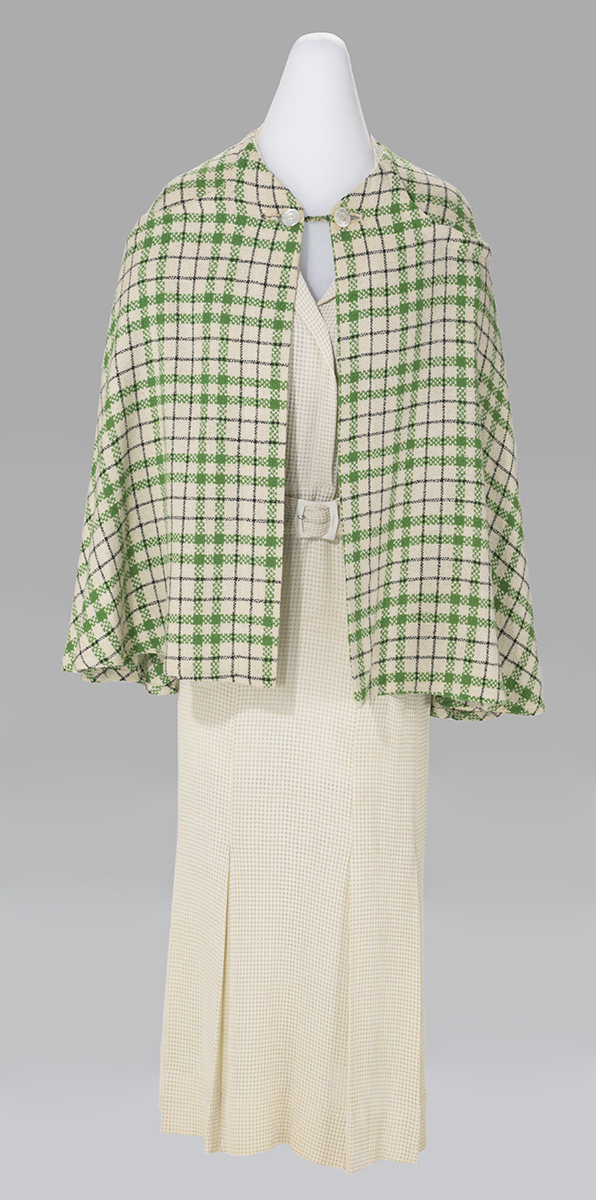 White dress with hip-length green-and-pink checked cape over it
