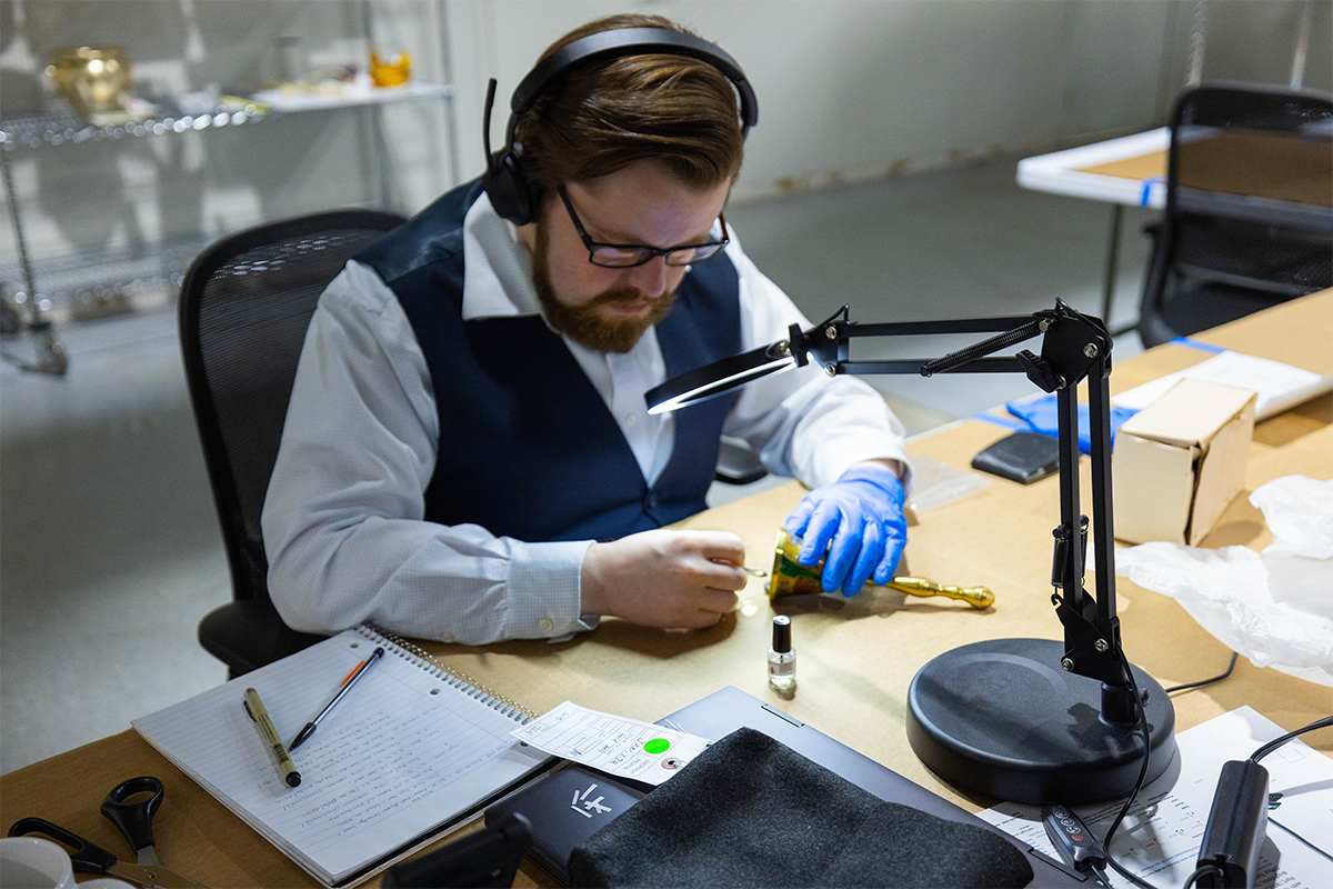 Artifacts in The Henry Ford collection are physically labeled with their accession number. A school bell from the Jackson Family Home is shown being labeled by Collections Specialist - Cataloger, Andrew Schneider. / Photo by Staff of The Henry Ford.