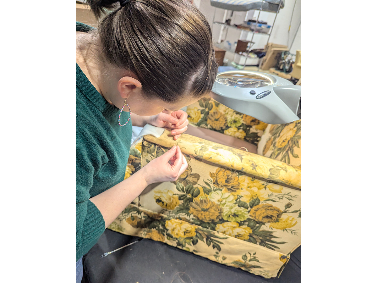 Associate Conservator Kate Herron adds netting to the arms of this Floral Globe Furniture Company armchair, an object used in the Jackson Family Home, for extra stability. / Photograph by Staff of The Henry Ford. 